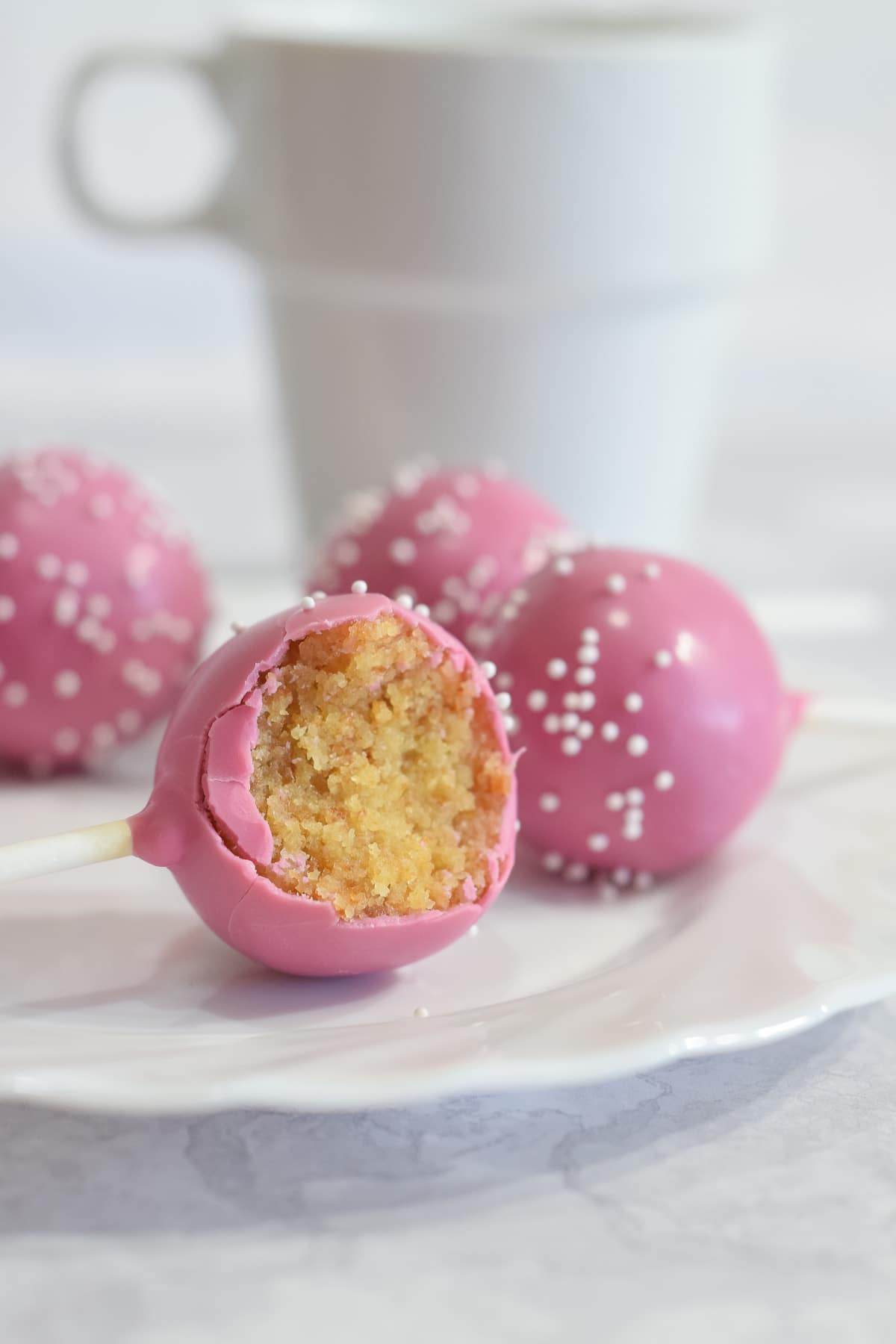 Pink Starbucks copycat vanilla birthday cake pops with white mini pearl sprinkles showing inside on plate