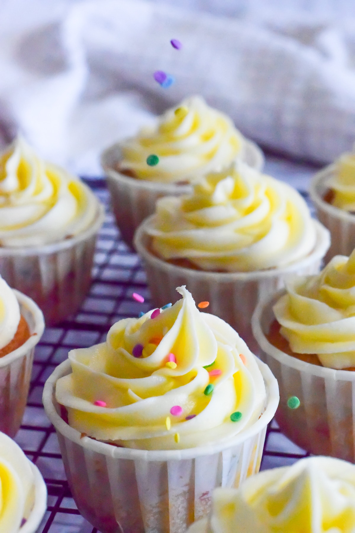 vanilla funfetti cupcakes with confetti sprinkles inside and being sprinkled on top of vanilla buttercream