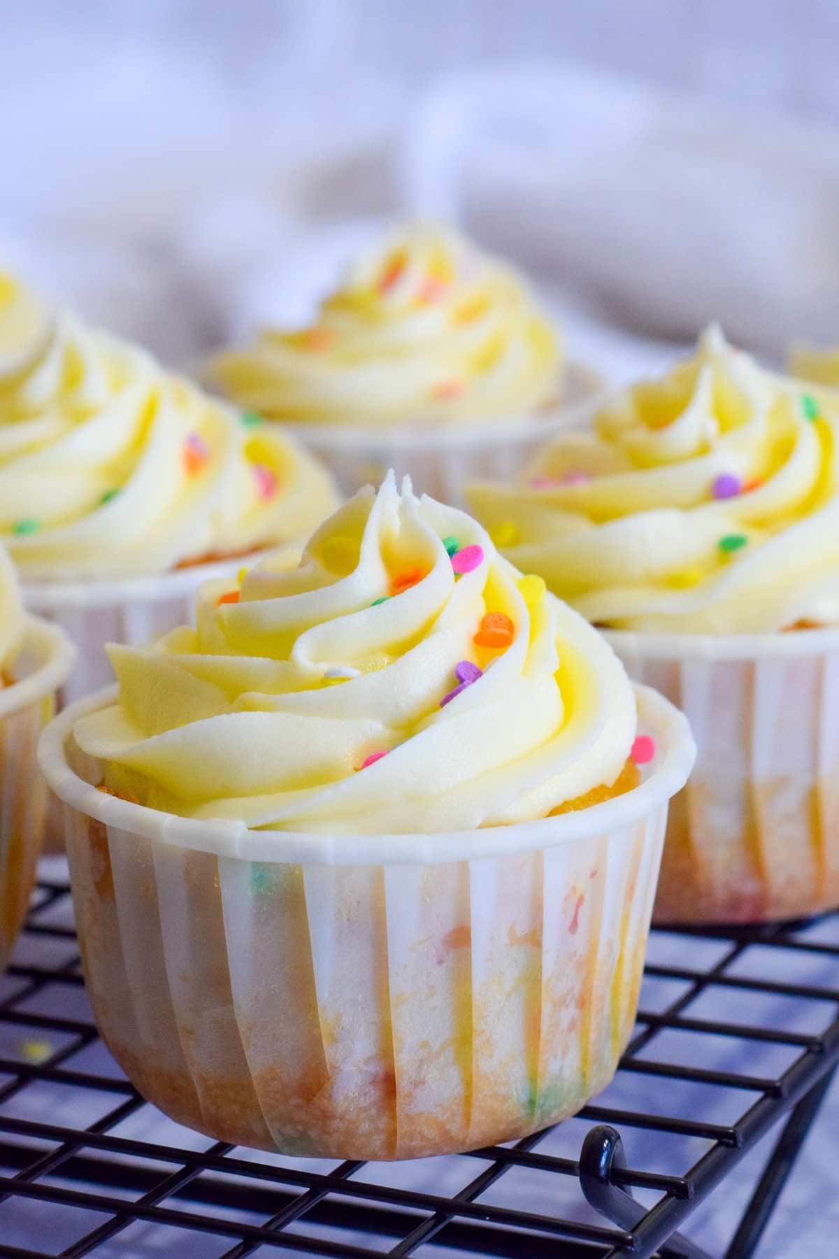 vanilla funfetti cupcakes in baking cups with confetti sprinkles inside and on top of vanilla buttercream