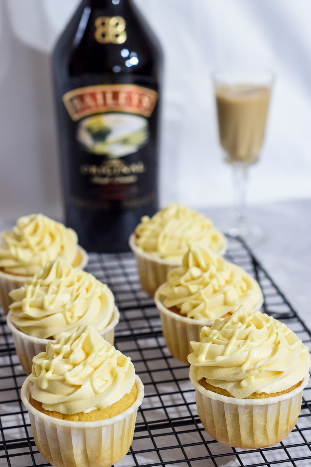 Bailey's Irish cream liqueur cupcakes with Bailey's frosting and white choc drizzle on rack with bottle of Baileys behind