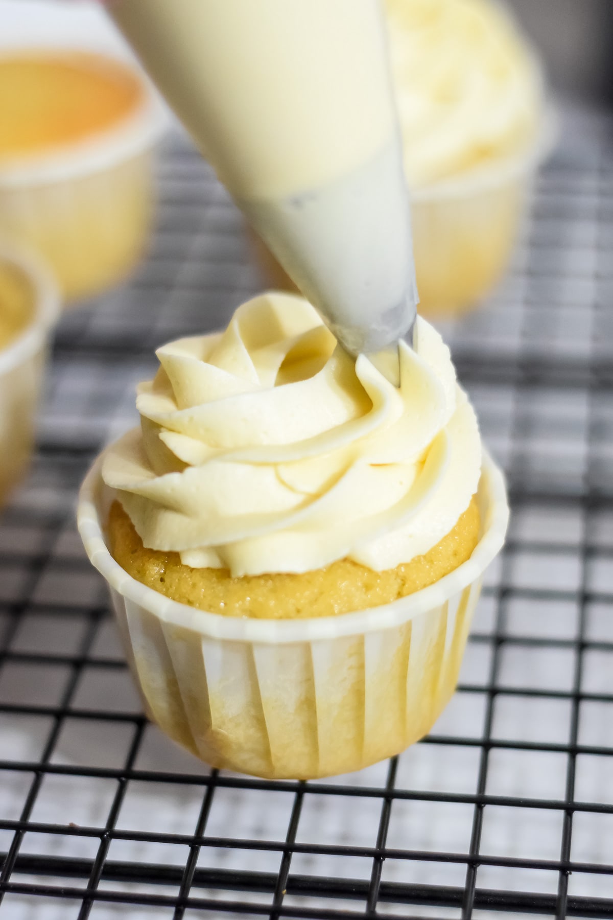 Baileys irish cream frosting piped from a piping bag onto a cupcake on a wire rack