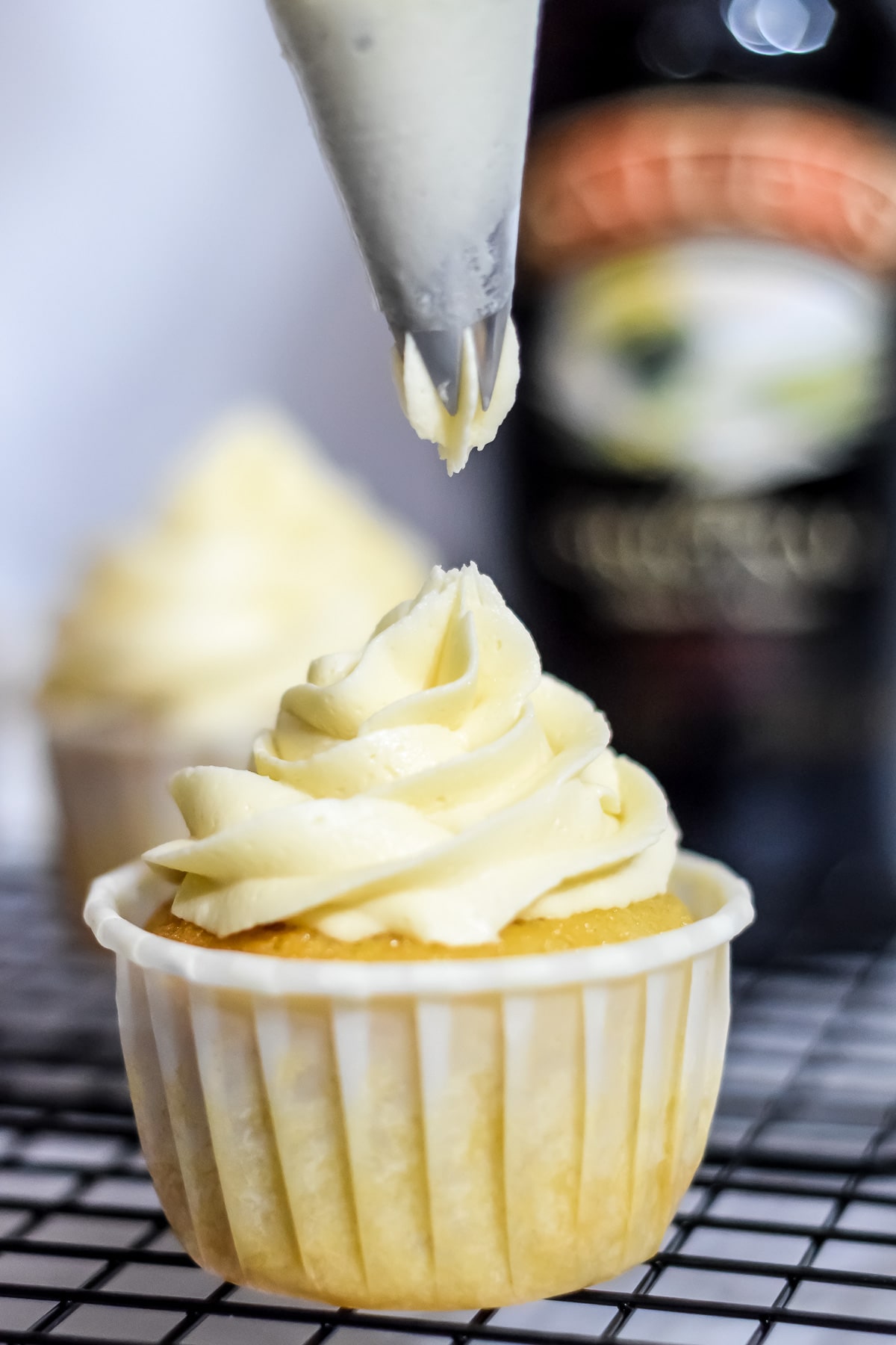 Irish cream frosting piped onto a cupcake with Baileys bottle behind
