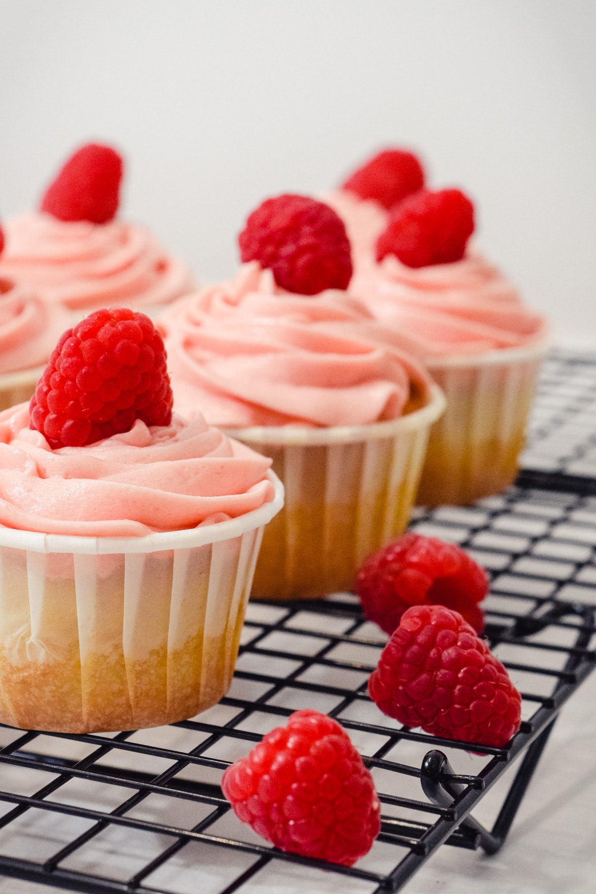 vanilla raspberry cupcakes with fresh raspberries on wire rack