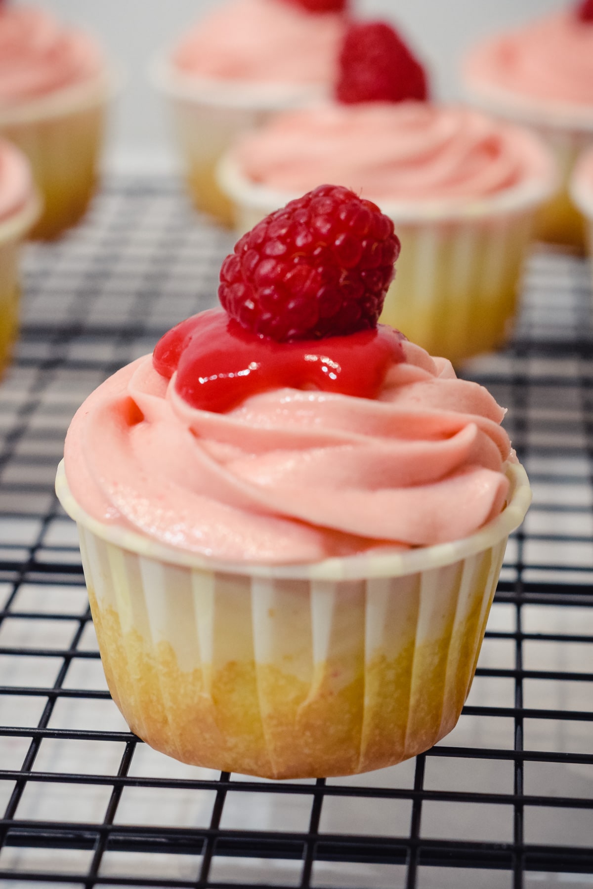 vanilla raspberry cupcake with raspberry puree reduction sauce and fresh raspberry on top.