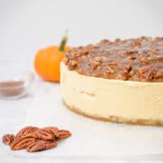 Pumpkin spice cheesecake with pecan praline topping side view with pecans in front and pumpkin behind