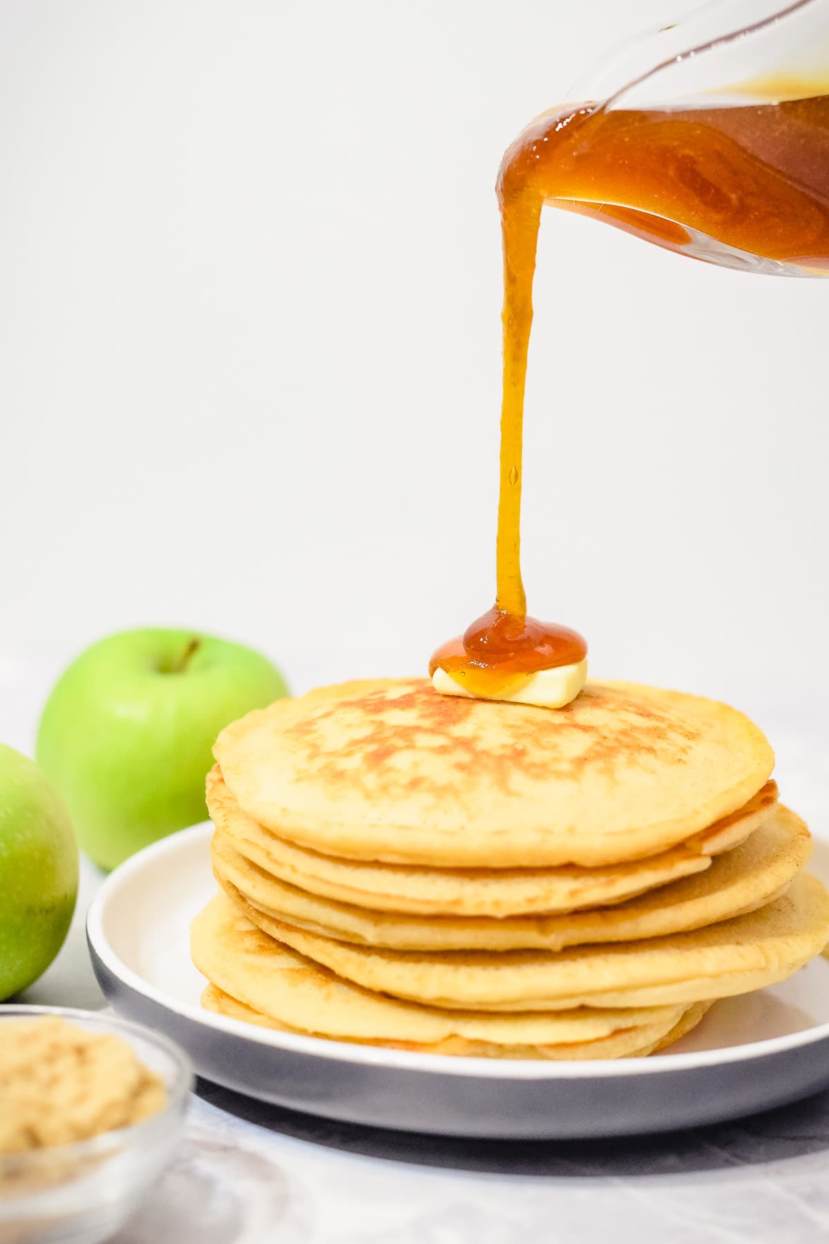 apple syrup poured from jug onto pancakes