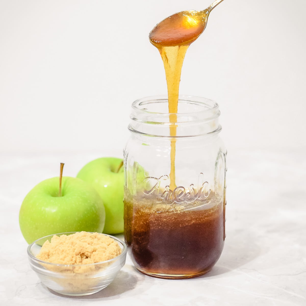 apple syrup poured from spoon into mason jar with real apples and brown sugar