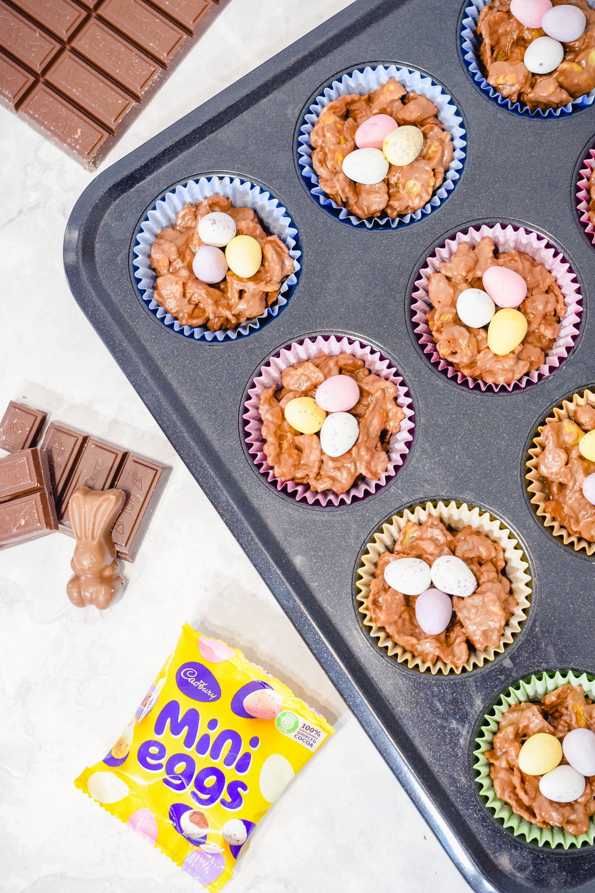 Easter chocolate cornflake nest cakes in cupcake liners in a muffin tin and topped with mini eggs