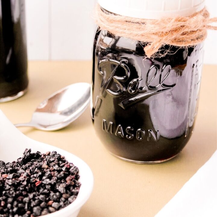 eldeberry syrup in a jar next to cup of elderberries