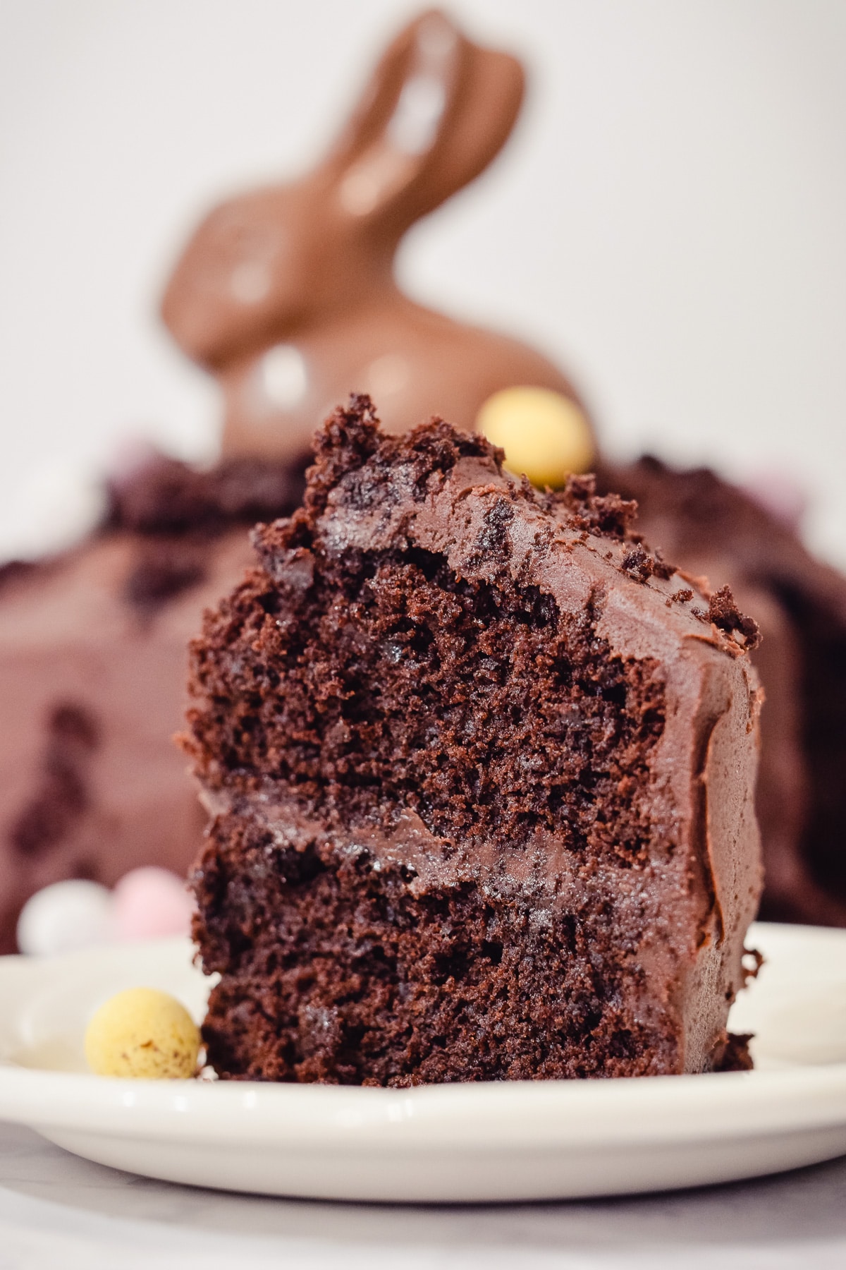 Slice of moist Easter chocolate mud cake with a chocolate rabbit in a cake in the background