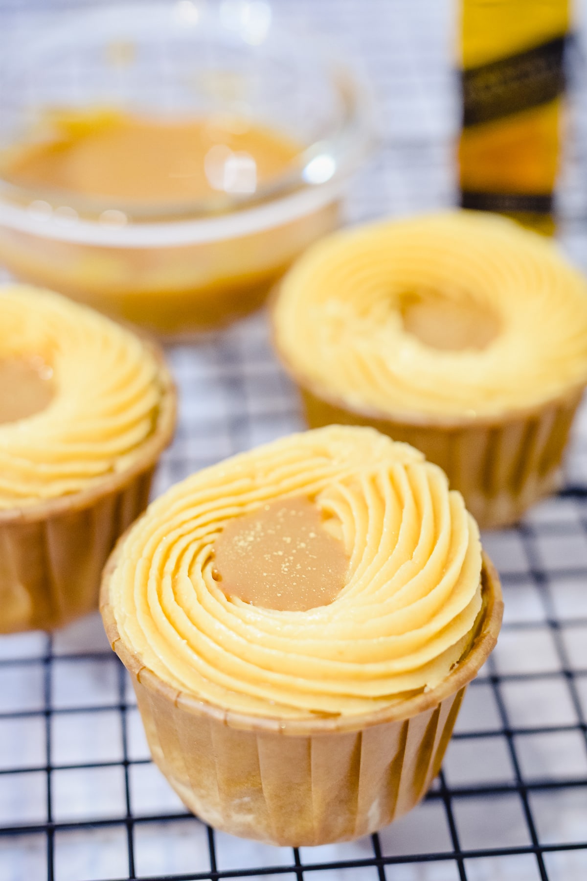 salted caramel whiskey cupcakes on wire rack with a whisky bottle and caramel in a bowl