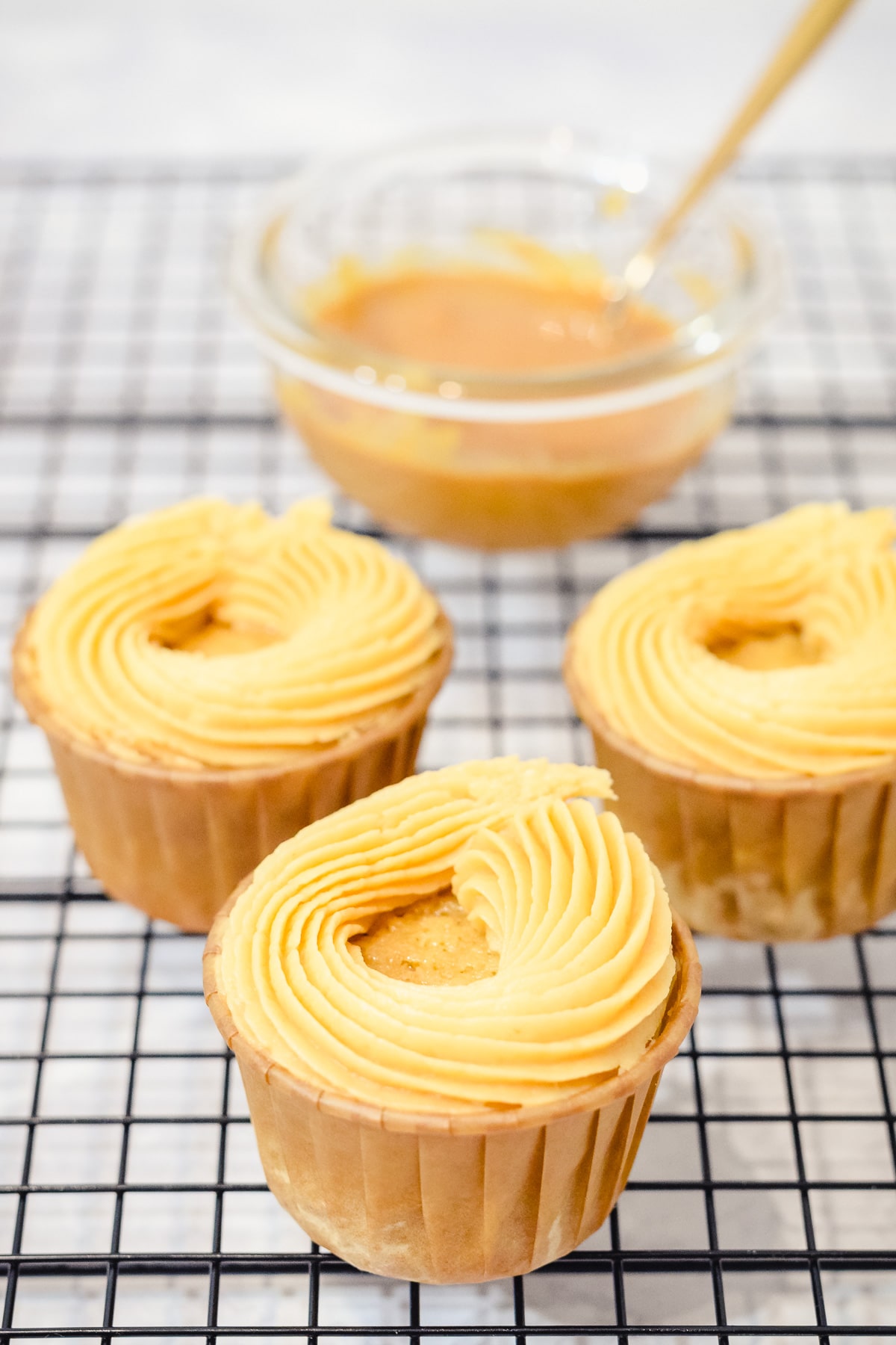 caramel buttercream frosting swirls on cupcakes with a bowl of store-bought caramel behind