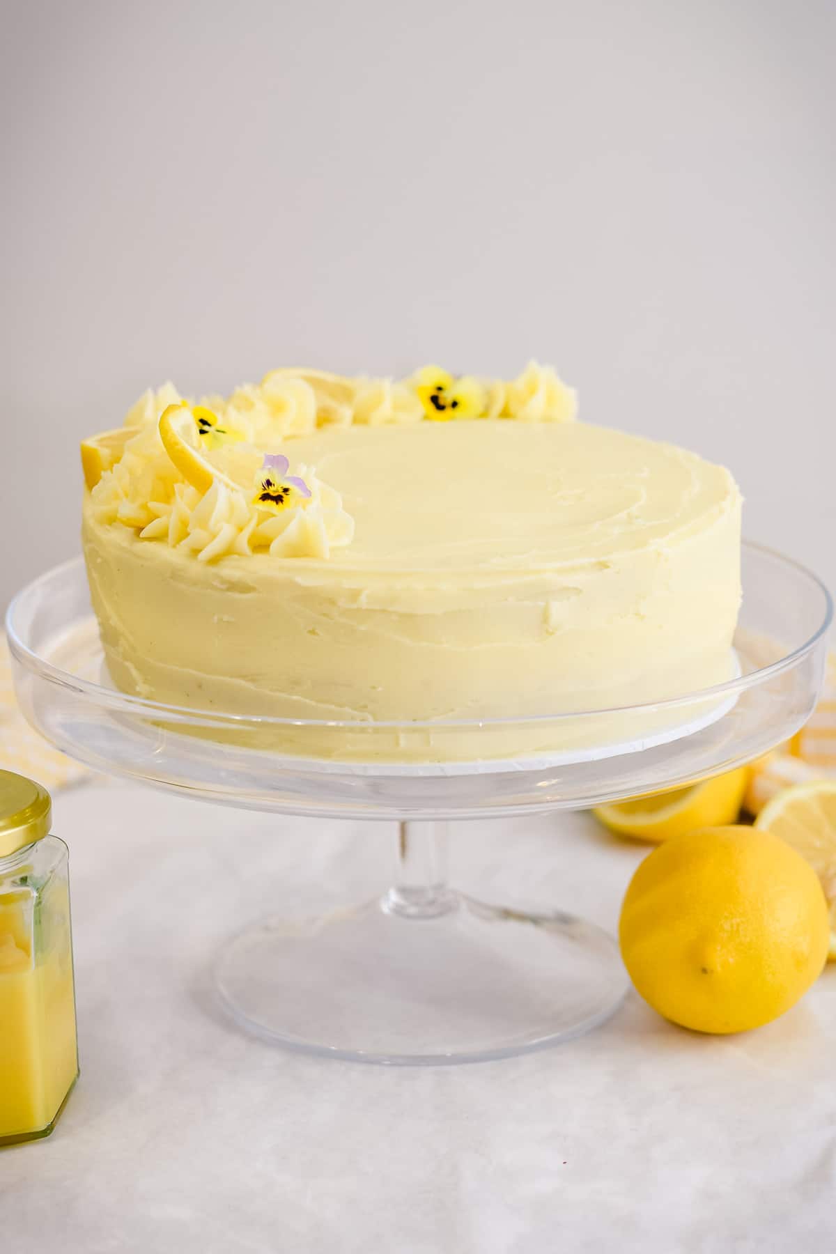 lemon curd cake on a cake stand with lemon curd and lemons
