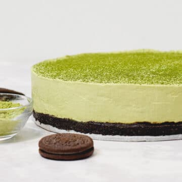 matcha green tea cheesecake with matcha powder dusted on top and oreos in front with a bowl of matcha on the side