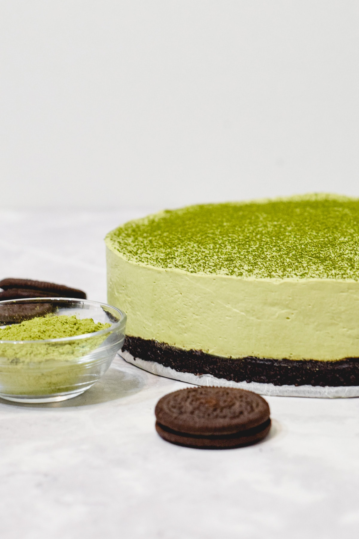 matcha green tea cheesecake side view with oreos and a bowl of matcha powder on the table