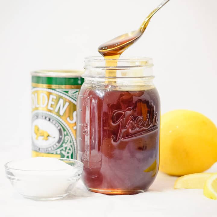 homemade golden syrup in a jar with sugar and lemon behind and a drizzling spoonful