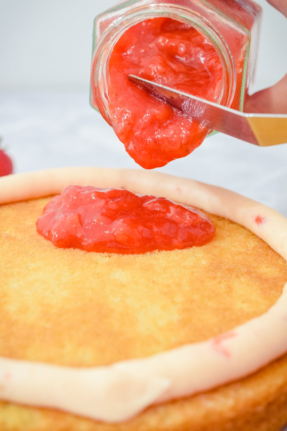 homemade strawberry cake filling sauce being poured onto a cake layer from a jar