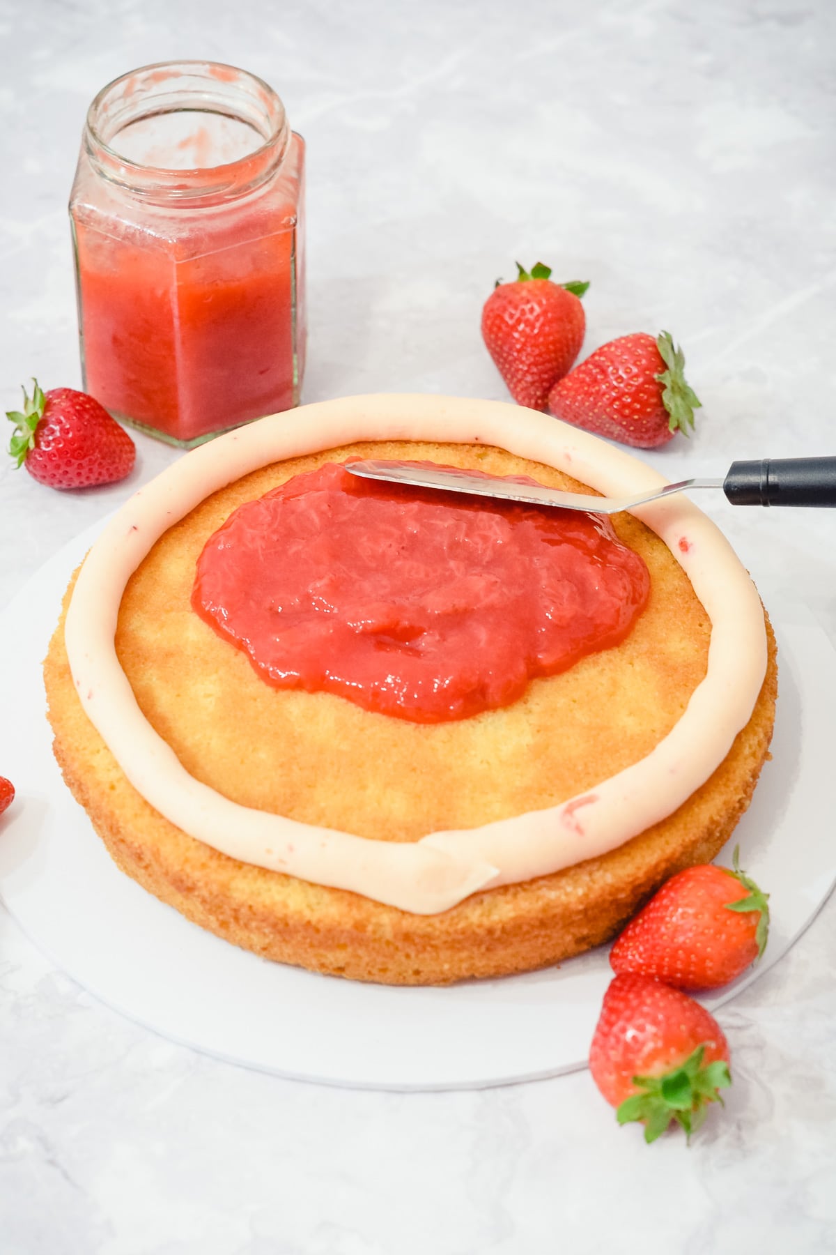 strawberry cake filling sauce being spread onto a cake layer with a jar of strawberry filling behind