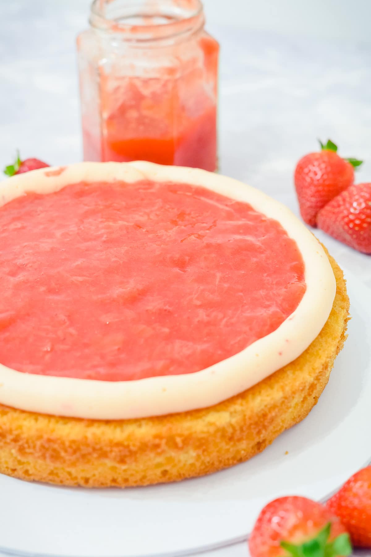 strawberry cake filling sauce spread onto a cake layer inside a ring of frosting