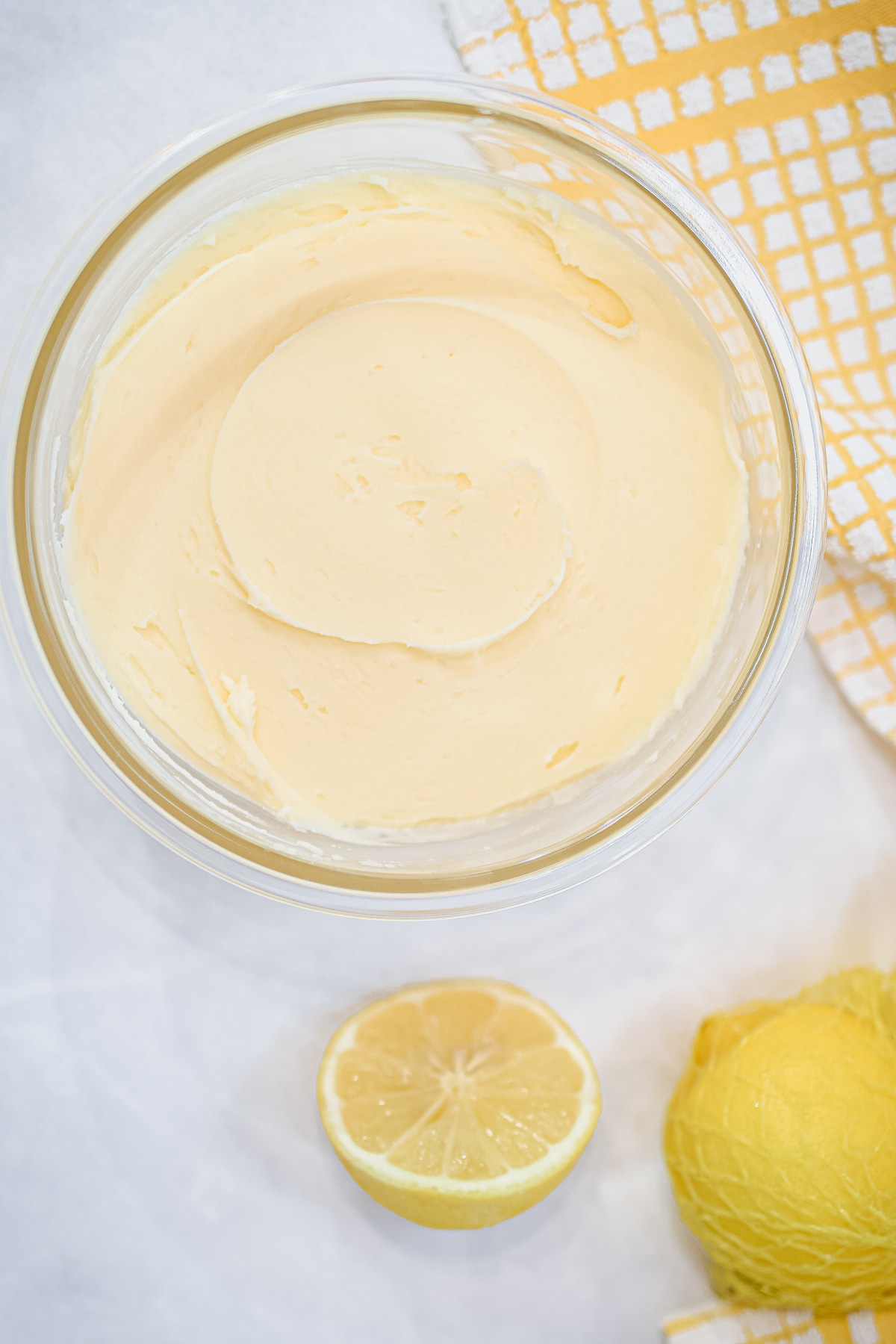 easy lemon buttercream frosting in a mixing bowl with lemons and yellow tea cloth behind