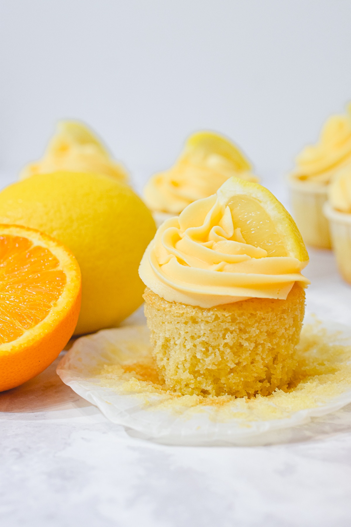 lemon cupcake with orange buttercream and a lemon slice and fresh lemon and fresh orange behind