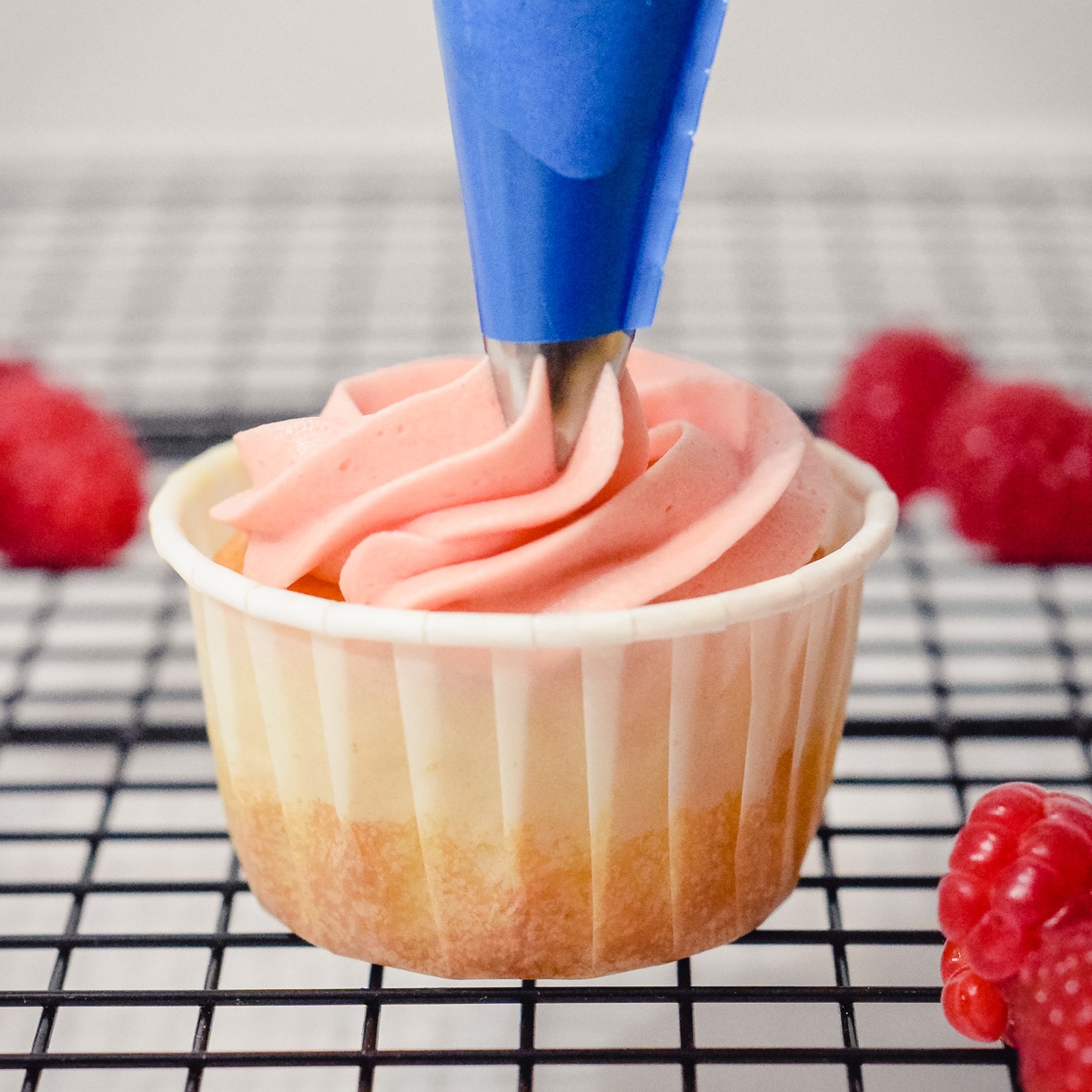 homemade raspberry buttercream piped onto a cupcake with fresh raspberries around it