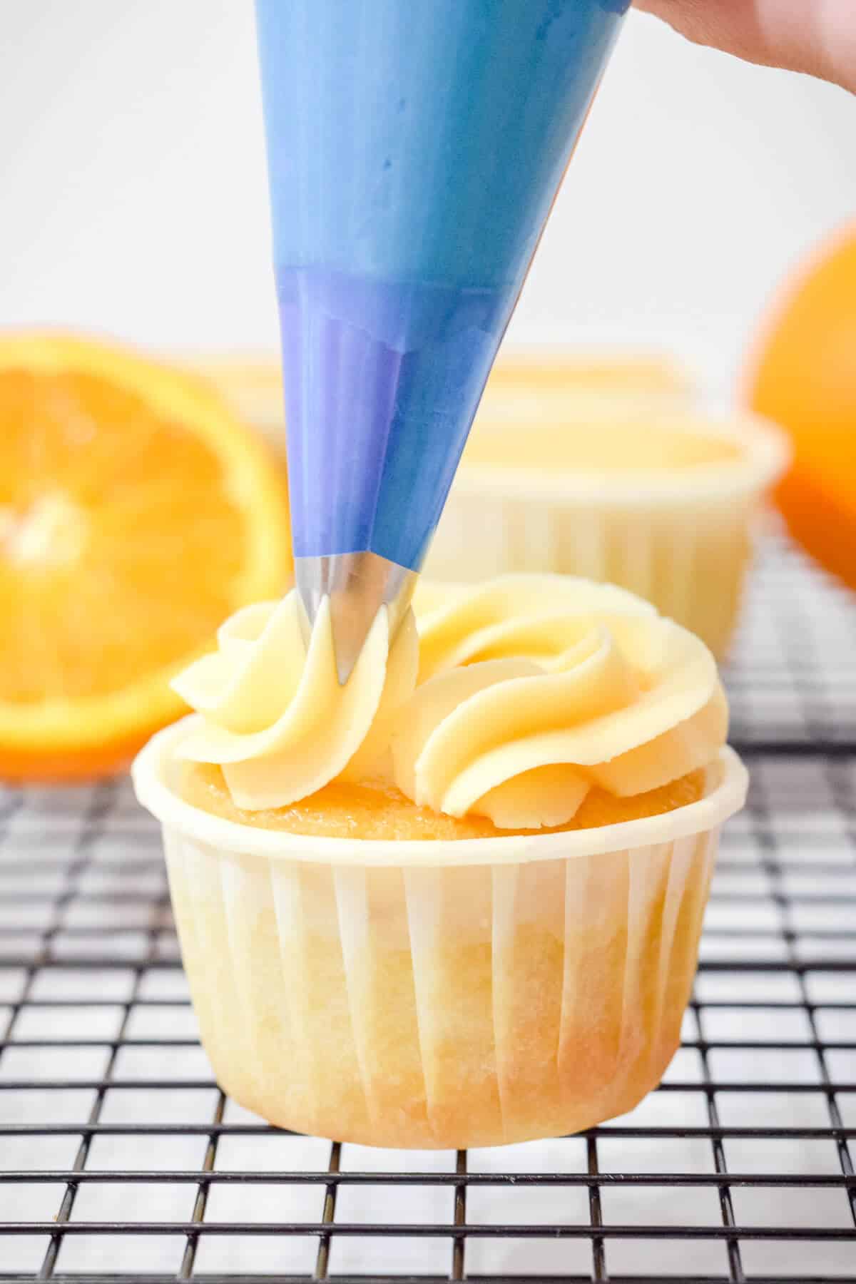 orange buttercream being frosted onto a cupcake