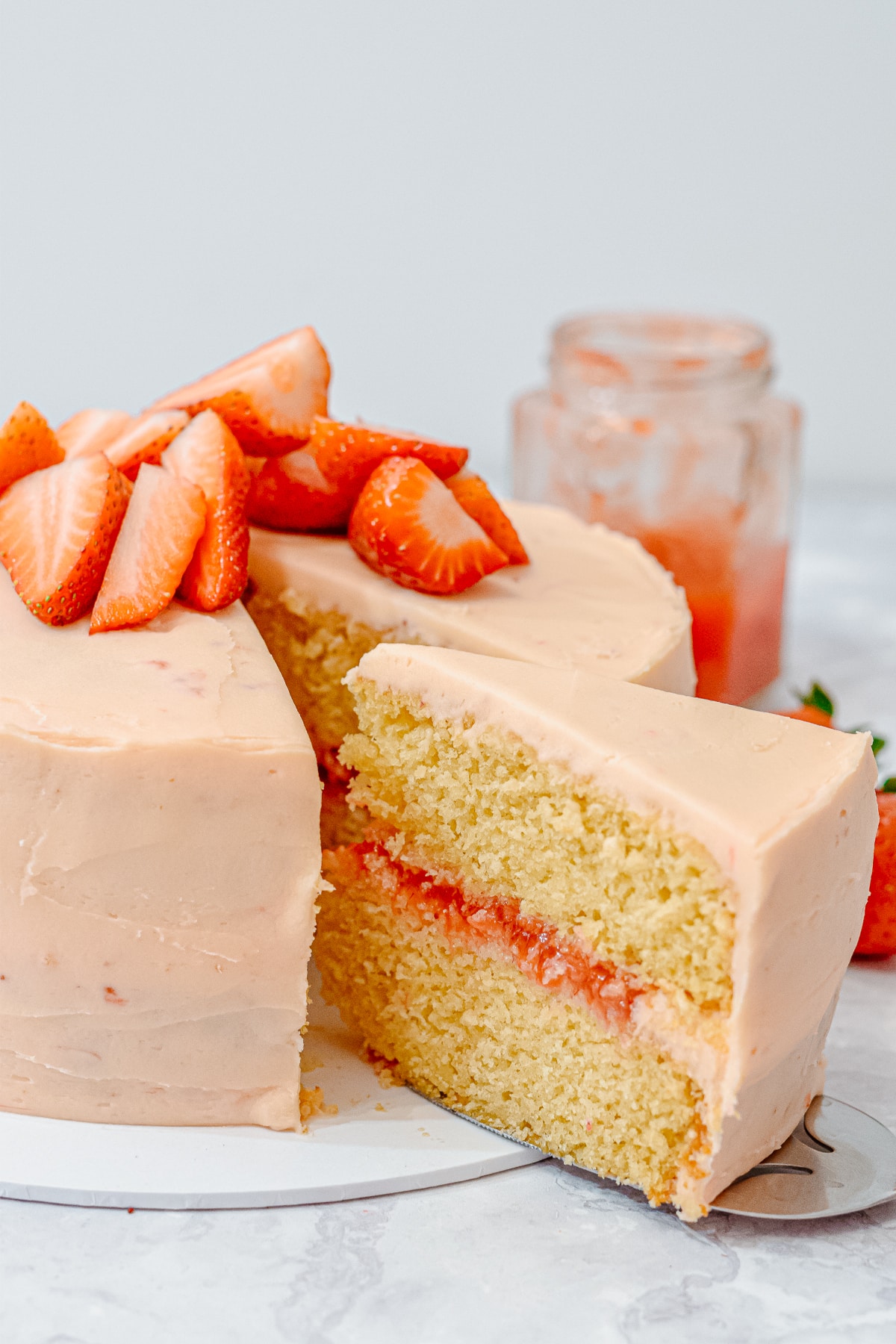 pink strawberry vanilla layer cake with a slice taken out showing strawberry filling and strawberry frosting, topped with fresh strawberries
