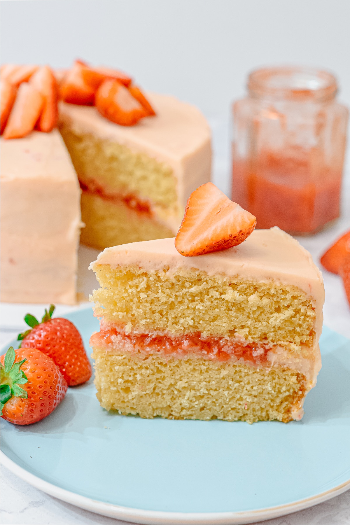 A slice of strawberry vanilla layer cake showing homemade strawberry cake filling between the layers and topped with strawberries