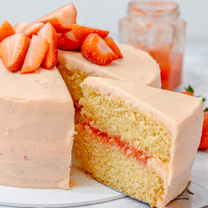 pink strawberry vanilla layer cake with a slice taken out showing strawberry filling and strawberry frosting, topped with fresh strawberries
