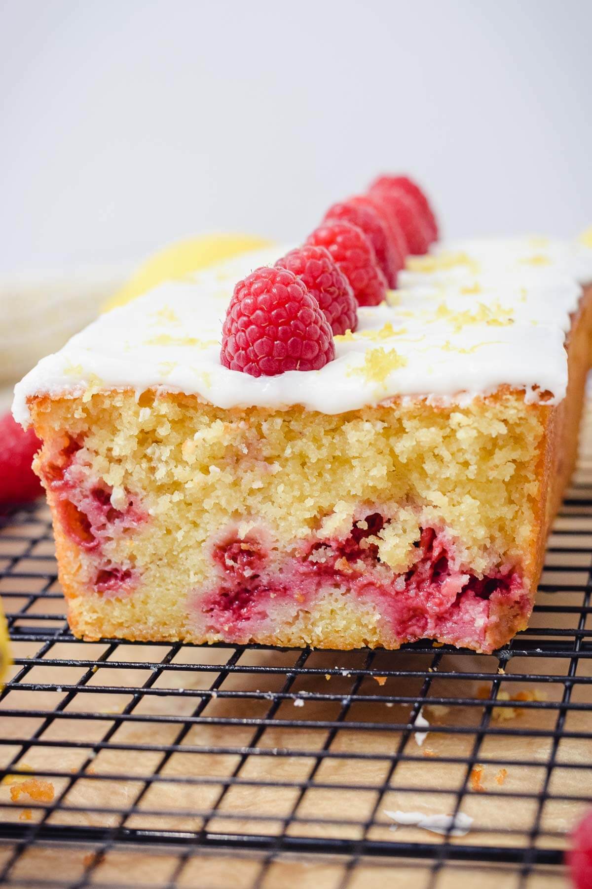 lemon raspberry loaf pound cake sliced topped with lemon glaze and fresh raspberries