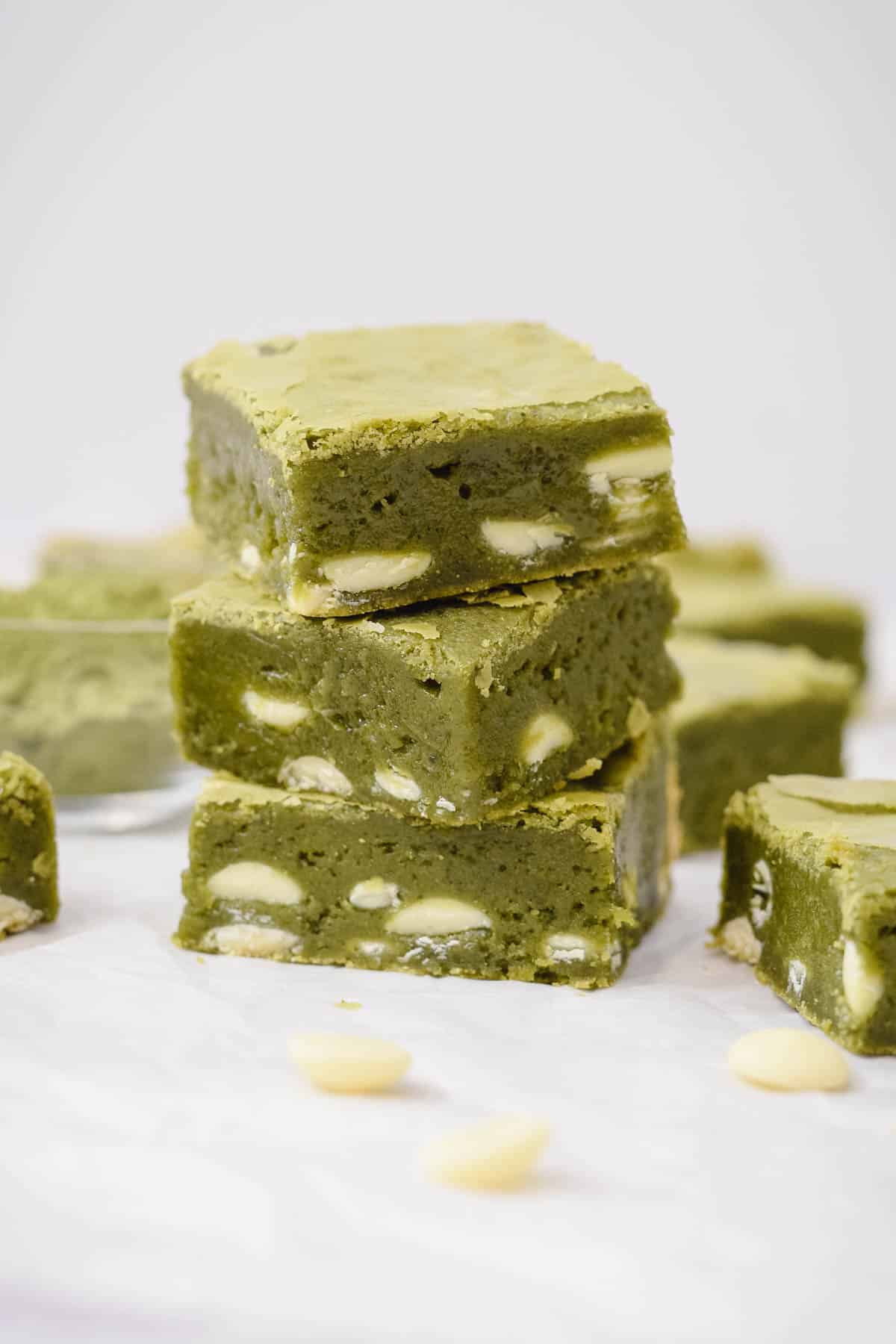 green tea matcha brownies in squares stacked on top of each other with white chocolate chips scattered