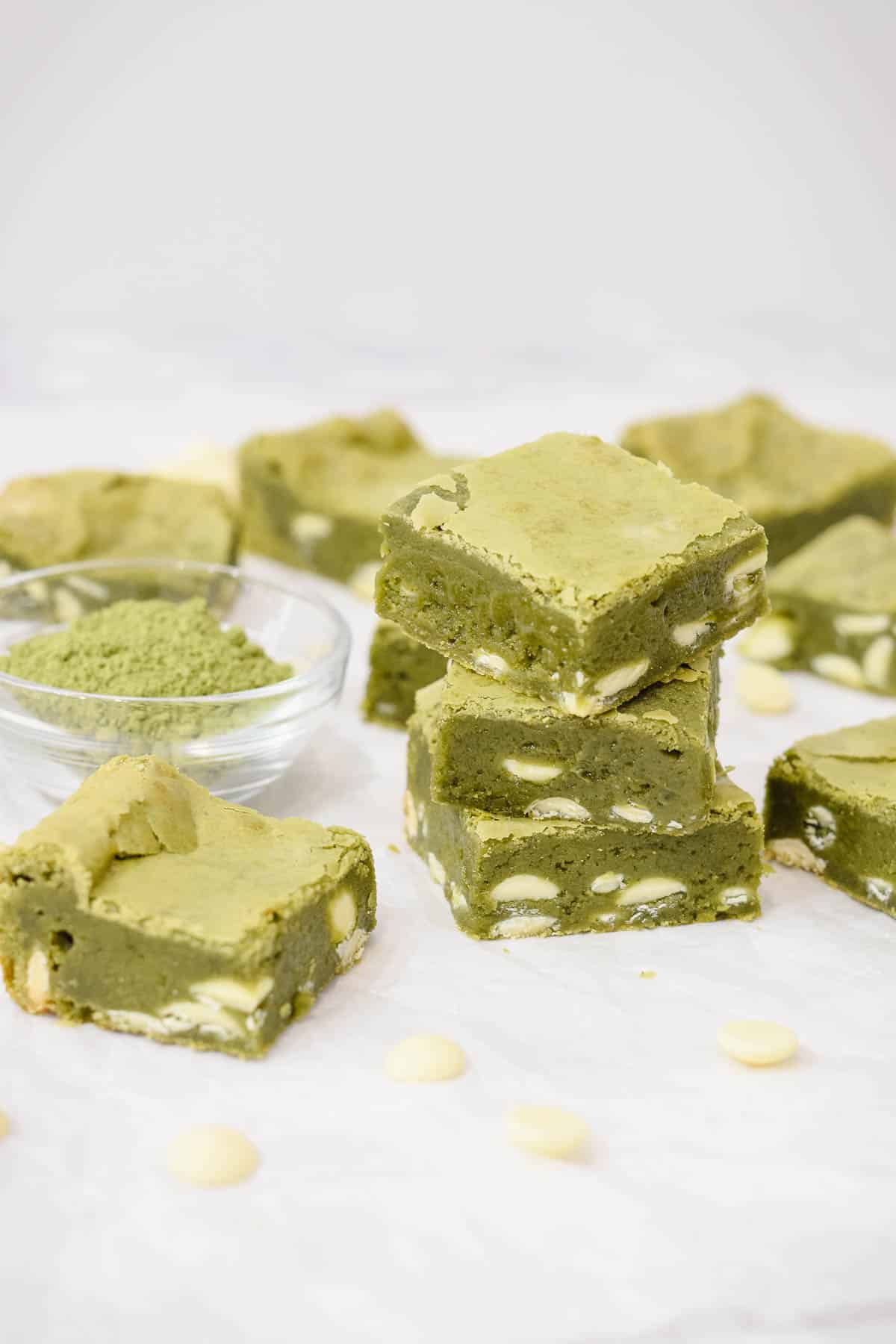 green tea matcha brownies squares stacked with white chocolate chips scattered and a bowl of matcha powder