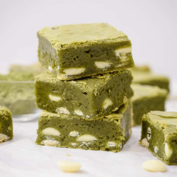 green tea matcha brownies in squares stacked on top of each other with white chocolate chips scattered