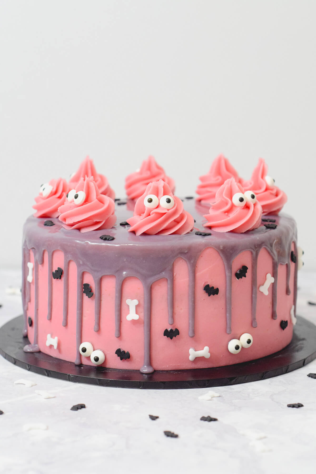 pink halloween cake with a purple ganache drip decorated with sprinkles and pink monsters.