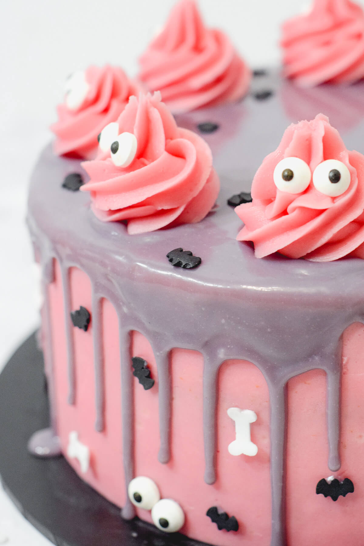 close up side view of a pink halloween cake with a purple drip with sprinkles and pink monsters.