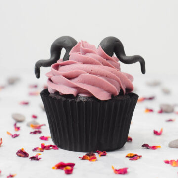 halloween disney dusky pink and chocolate maleficent cupcake with edible black horns topper and dried rose petals scattered.