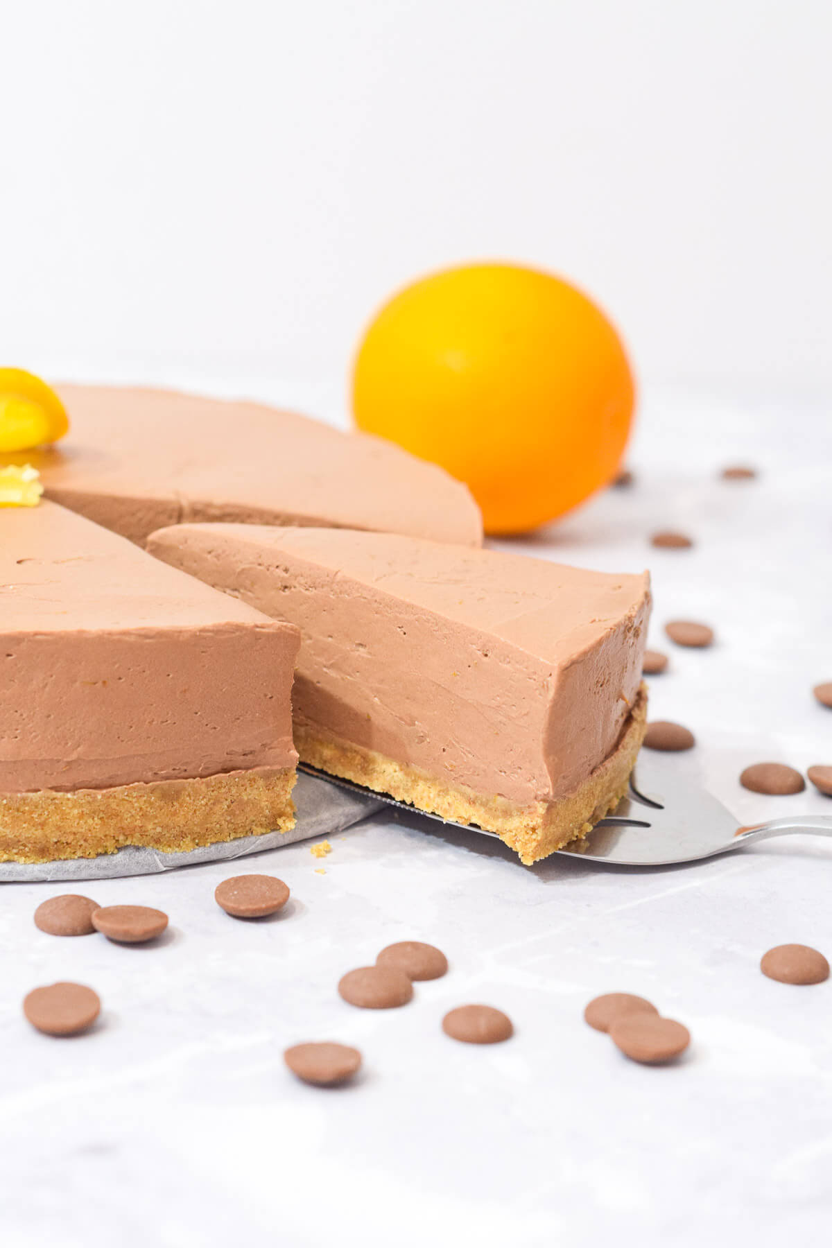 chocolate orange cheesecake with a slice being pulled out and a whole orange behind.