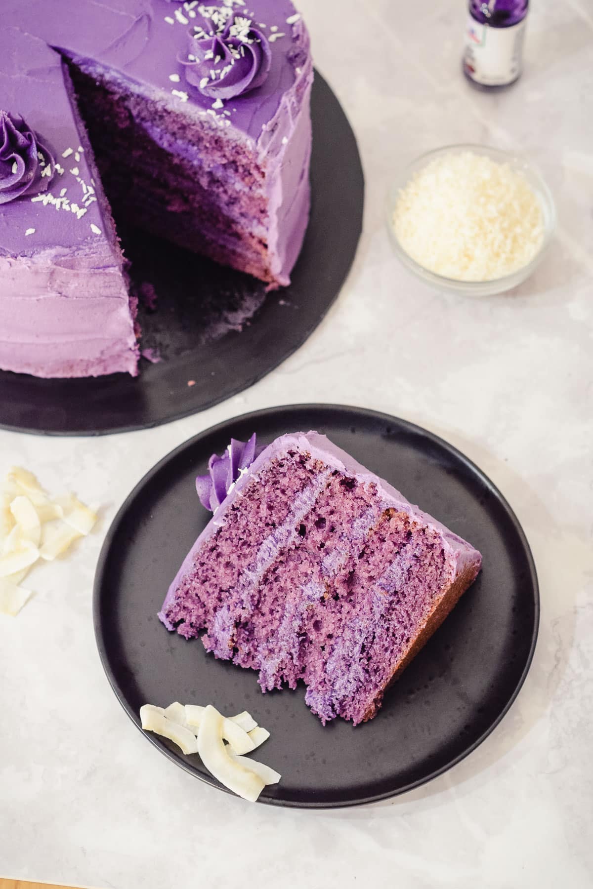 slice of purple yam ube cake with four layers of ube sponge and an ube frosting and coconut topping.